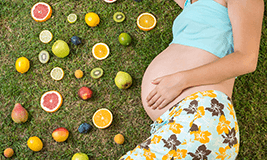 pregnant woman laying on grass with fruits around her