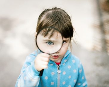 Young girl in raincoat holding magnifying glass to eye