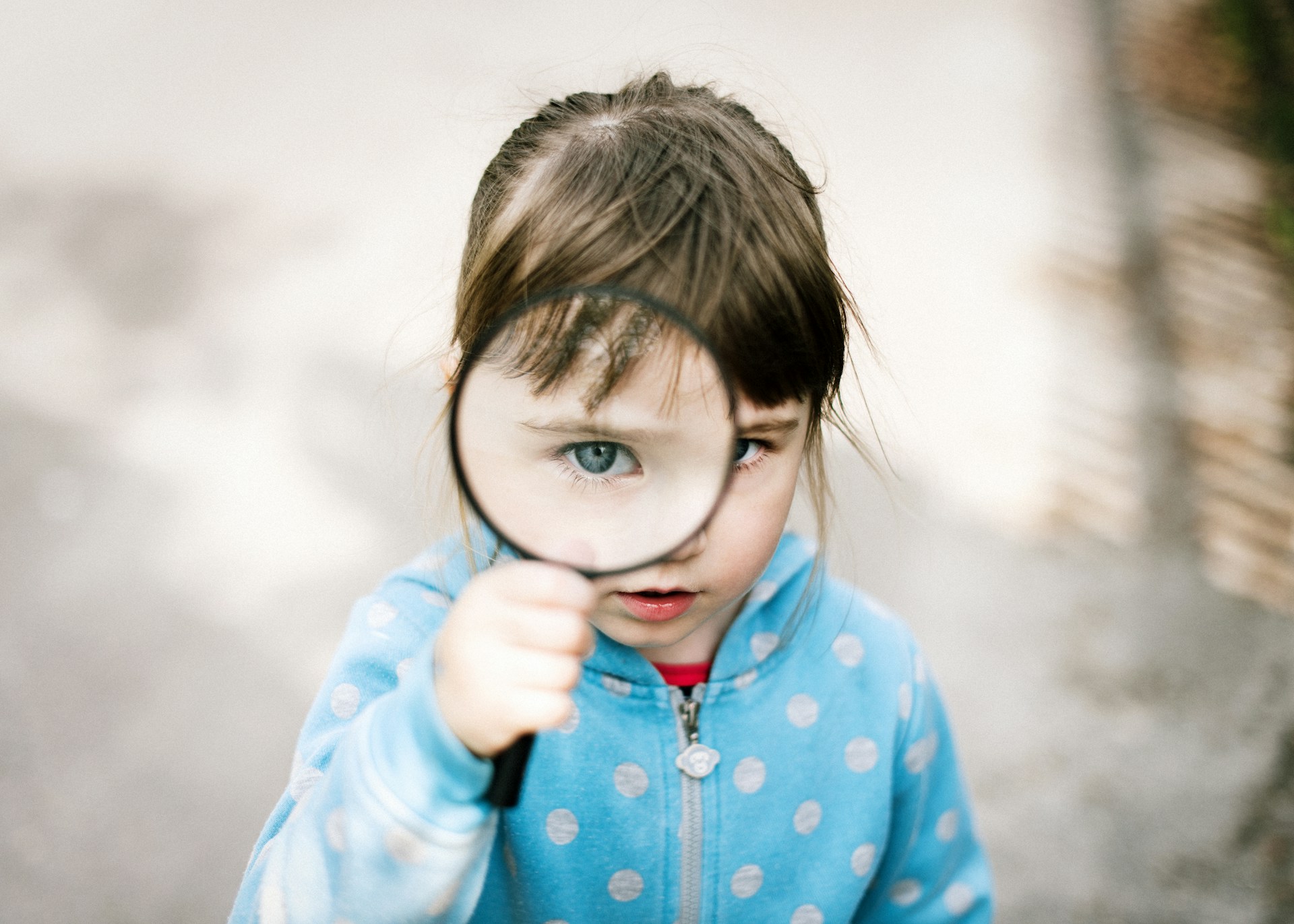 Young girl in raincoat holding magnifying glass to eye