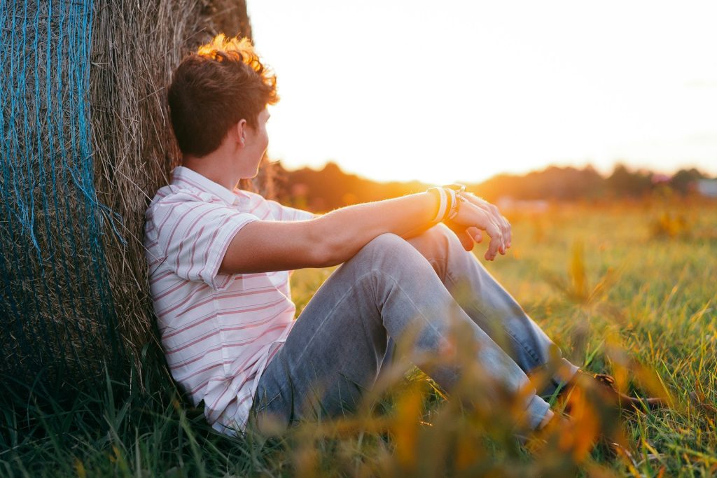 Boy sitting in a field at sunset looking away
