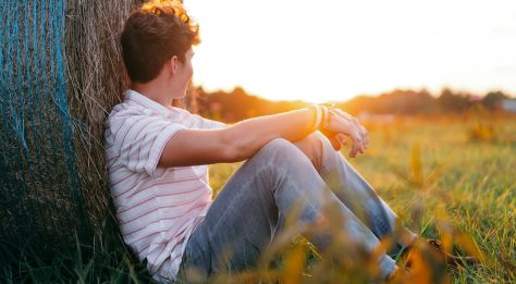 Boy sitting in a field at sunset looking away