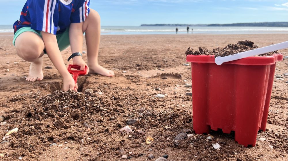 child on beach digging in sand with bucket