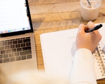 person writing in a notebook with laptop