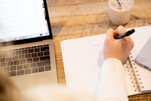 person writing in a notebook with laptop