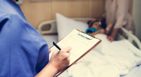 close up of clipboard saying 'doctor's visit' with blurred child in hospital bed in background